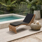 Wave Sun Lounger on a wooden deck by the pool, black cushion, woven frame amid tropical plants