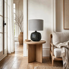 Aksel Table Lamp in Slate with ribbed ceramic base and linen shade sits on wood side table in bright living room.