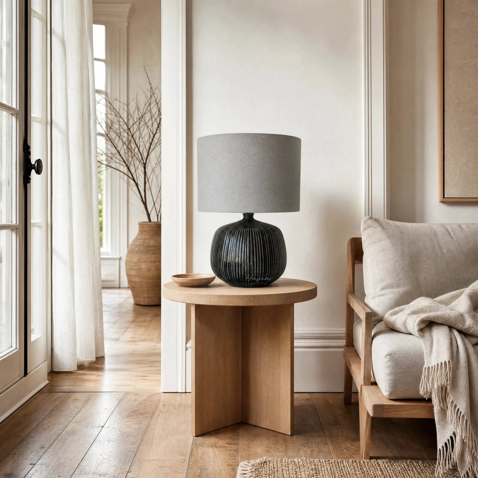 Aksel Table Lamp in Slate with ribbed ceramic base and linen shade sits on wood side table in bright living room.